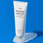 Un tube blanc de Jumiso Nettoyant Moussant Purifiant Anti Imperfections à l'Acide Salicylique 120 g se tient debout sur une tache de nettoyant avec un emballage et une marque minimes, sur fond bleu. Dakar