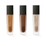 Trois flacons de fond de teint Lancome Fond De Teint Tenue 24h Fini Mat Naturel SPF35, chacun avec un bouchon noir et un flacon en verre dépoli, sont présentés côte à côte sur un fond blanc dans différentes nuances. Dakar