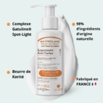 Un flacon de 500 ml d'Oxyprolane Lait éclaircissant taches – éclat du teint est posé sur un fond de teint crème. Il contient le complexe Gatuline Spot-Light, 98 % d'ingrédients d'origine naturelle et du beurre de karité. Fabriqué en France. Dakar