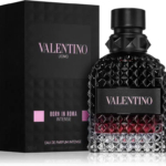 Un flacon du parfum Valentino Uomo Born in Roma Intense est présenté devant son emballage noir. Le flacon présente une surface sombre et texturée, avec un dégradé allant du bordeaux profond au noir, et le nom de la marque y est bien visible. Dakar