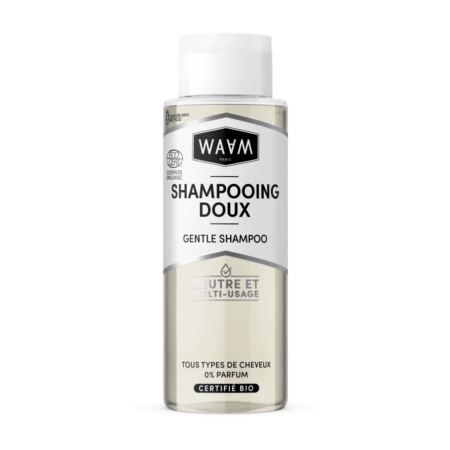 Un flacon transparent de shampoing doux WAAM Paris avec un bouchon argenté. L'étiquette, en français et en anglais, souligne sa certification biologique et son adéquation à tous les types de cheveux. Le texte indique sa neutralité et sa polyvalence. Dakar