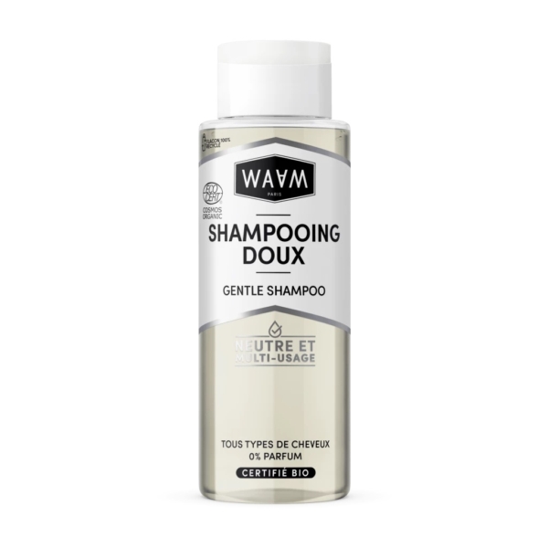 Un flacon transparent de shampoing doux WAAM Paris avec un bouchon argenté. L'étiquette, en français et en anglais, souligne sa certification biologique et son adéquation à tous les types de cheveux. Le texte indique sa neutralité et sa polyvalence. Dakar