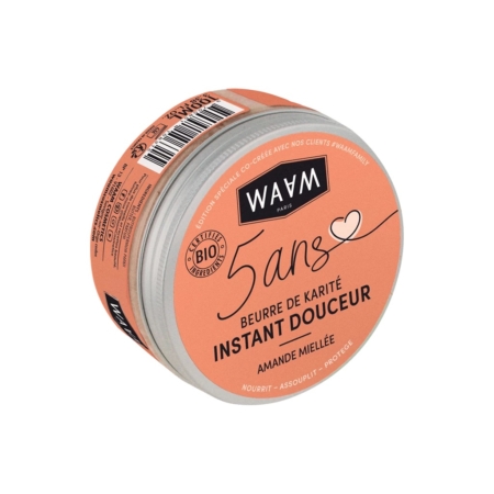 Un contenant rond orange portant l'inscription « WAAM Paris » avec les mentions « 5 ans » et « Beurre de Karité Instant Douceur » en noir. Il porte les certifications de production biologique et éthique. Au fond, on peut lire « Amande Miellée ». Dakar