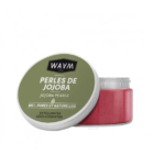 Un pot de Perles de Jojoba WAAM Paris, étiqueté « Perles de Jojoba ». Le couvercle est vert avec un texte noir et blanc. Le pot contient des perles exfoliantes roses, annoncées comme « 100 % pures et naturelles » et « exfoliantes adoucissantes ». Dakar