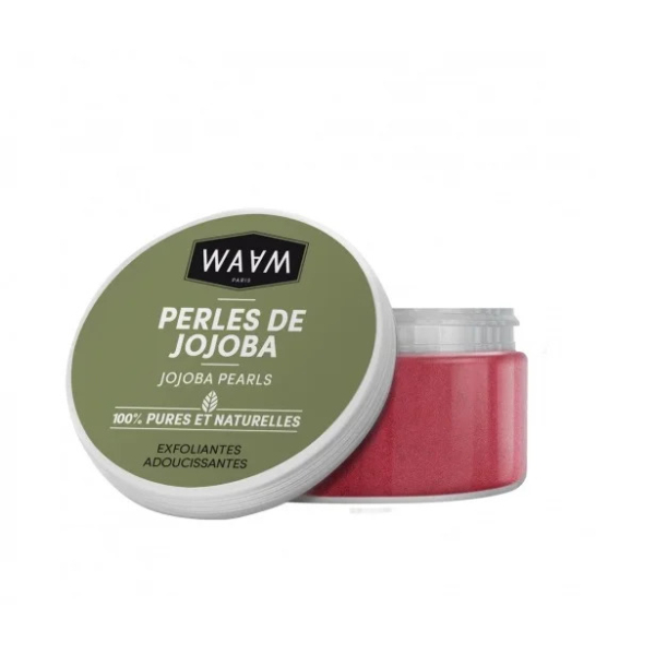 Un pot de Perles de Jojoba WAAM Paris, étiqueté « Perles de Jojoba ». Le couvercle est vert avec un texte noir et blanc. Le pot contient des perles exfoliantes roses, annoncées comme « 100 % pures et naturelles » et « exfoliantes adoucissantes ». Dakar