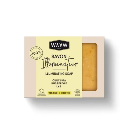 Un pain de savon rectangulaire présenté dans une boîte étiquetée « WAW » avec l'inscription « Savon Illuminateur » et les ingrédients suivants : « Curcuma, Busserole, Lys ». L'emballage indique qu'il est 100 % naturel et convient aux soins « Visage et Corps ». Dakar