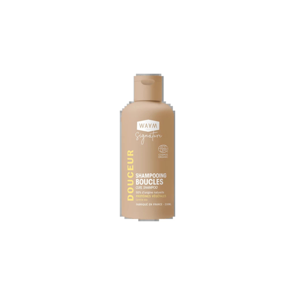 Un flacon de shampoing Wavy Signature Douceur Boucles. Le flacon est de couleur beige clair avec un texte doré. Spécialement formulé pour les boucles, il contient des ingrédients d'origine végétale. Le flacon de 230 ml est fabriqué en France. Dakar