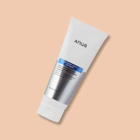 Un tube d'Anua Nettoyant Moussant Doux Hydratant à l'Acide Hyaluronique 150 ml s'affiche sur fond pêche, présentant un motif blanc et argenté avec un étiquetage bleu à côté de l'Anua Mousse Nettoyante en Profondeur. Dakar