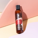 Une bouteille brune d'Asiam Après Shampooing sans Rinçage 237 ml avec un bouchon noir repose sur un fond pastel de surfaces courbes rose doux, pêche et beige. Dakar