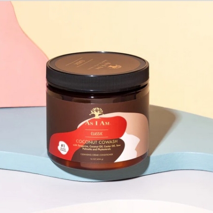 Un pot d'Asiam Cache-cache à la noix de coco 16 onces avec un couvercle noir et une étiquette rouge, beige et marron repose sur une surface pastel avec des formes abstraites en arrière-plan, soulignant son soin nourrissant. Dakar
