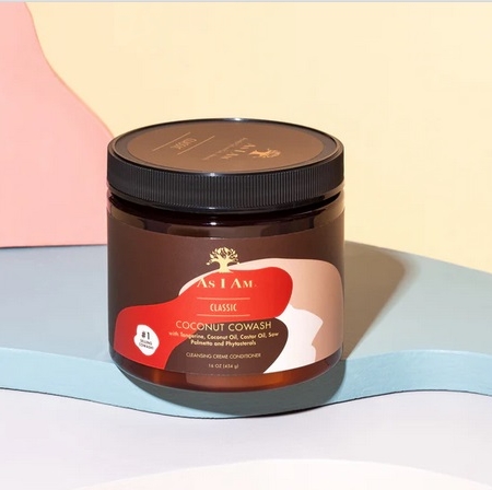 Un pot d'Asiam Cache-cache à la noix de coco 16 onces avec un couvercle noir et une étiquette rouge, beige et marron repose sur une surface pastel avec des formes abstraites en arrière-plan, soulignant son soin nourrissant. Dakar