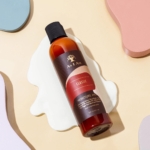 Une bouteille d'Asiam Lait-d'Hydratation 237 ml repose sur une surface beige avec des formes pastel abstraites et un liquide blanc renversé en dessous. Dakar