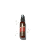 Un flacon pulvérisateur marron étiqueté « Asiam Spray contre la Cocoshea 120 ml » est placé au centre sur un fond blanc, avec de petites gouttes de liquide à proximité. Ce spray hydrate et rafraîchit les cheveux sans rinçage. Dakar