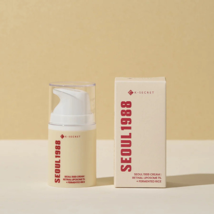 Un flacon de couleur crème avec une pompe blanche et un texte rouge minimal, étiqueté « Ksecret Crème Seoul 1988 Liposome rétinien 1 % + Riz fermenté 50 ml », se dresse à côté de sa boîte sur une surface claire sur un fond beige. Dakar