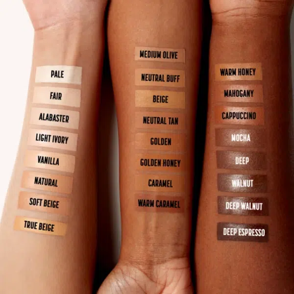 Trois avant-bras aux tons de peau différents présentent 18 échantillons de Nyx Anti Cernes Correcteur Longue Tenue Can't Stop Won't Stop 3,50 ml, étiquetés de « Pale » à « Deep Espresso », montrant un dégradé de nuances pour différents teints. Dakar