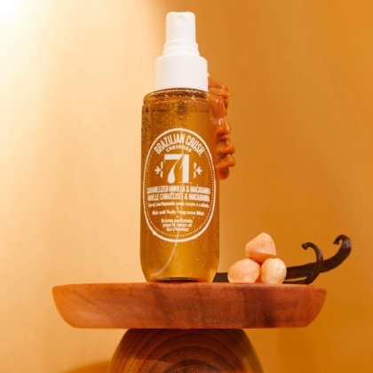 Un flacon Sol de Janeiro Brazilian Crush Cheirosa 71 Brume Parfumée 90 ml repose sur un piédestal en bois, entouré de caramel, de gousses de vanille et de noix de macadamia, sur un fond doré chaleureux. Dakar