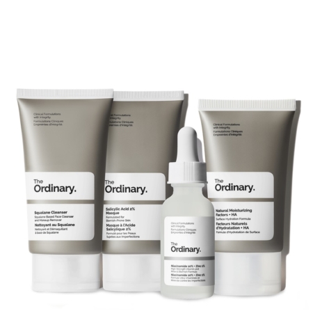 Trois produits de soin gris et blancs de The Ordinary The Balance Set Coffret Clarifiant Peaux à Imperfections — un nettoyant, une crème hydratante et un flacon compte-gouttes — sont exposés, chacun étiqueté avec les noms des produits et les ingrédients. Dakar