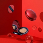 Un poudrier TirTir Fond Teint Fini Semi Mat Mask Fit Coussin Rouge 18 g, une houppette et des sphères transparentes flottent sur un fond rouge vif. Le poudrier ouvert dévoile son miroir et son fond de teint coussin. Dakar