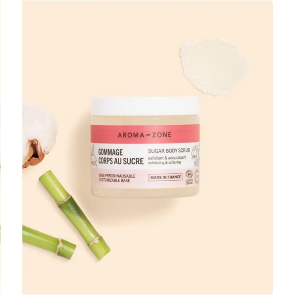Un pot de Gommage corps au sucre BIO Aroma Zone de 200 g repose sur une surface beige, avec une touche de ce gommage au sucre biologique à proximité. Le bambou et le coton évoquent ses ingrédients naturels, rappelant l'essence pure du Rituel de Sakura de Rituals. Dakar