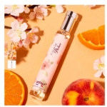 Un flacon d'Eau de parfum Fleur de pêcher 30 ml d'Adopte repose sur une surface aux tons pêche avec des tranches de pêche, une tranche d'orange et des fleurs roses, créant une ambiance douce et délicate semblable à Narciso Rodriguez POUDRÉE. Dakar