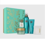Un coffret Rituals coffret moyen le rituel du karma sarcelle et or avec des motifs botaniques est présenté avec quatre articles de soin sarcelle et blanc : un pot, un flacon, un tube et une bougie. Dakar