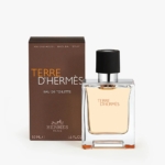 Un flacon de 50 ml de Hermès Terre d'Hermès se trouve à côté de sa boîte brune. Le flacon transparent à bouchon noir contient un liquide légèrement ambré. Le flacon et le coffret portent tous deux la marque Hermès Paris. Dakar