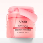 Un pot rose d'Anua Pads Anti Taches et Imperfections à la Niacinamide 5 TXA Brightening présente un tampon soulevé et une étiquette portant la mention "NIACINAMIDE 5 + TXA," contenant 60 tampons (210 ml/7.10 fl oz). Dakar