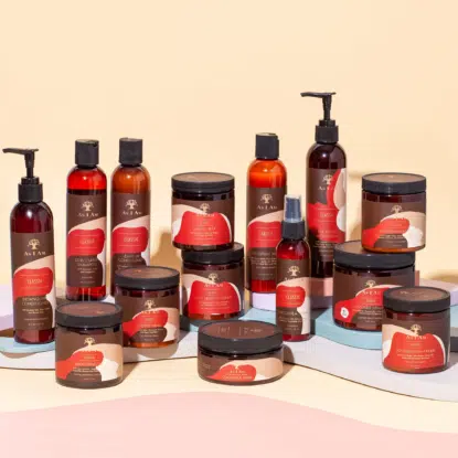 Une collection de produits capillaires As I Am Classic d'Univers Cosmetix, comprenant des flacons, des pots et des vaporisateurs, est disposée sur une surface de couleur pastel avec un fond beige. Dakar