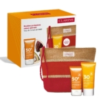 Le Coffret Clarins comprend la Crème Solaire Visage SPF50 (50ml), la Crème Solaire Corps SPF30 (75ml) et une pochette tressée rayée rouge et beige, le tout présenté dans une boîte orange avec des informations et des images sur le produit. Dakar