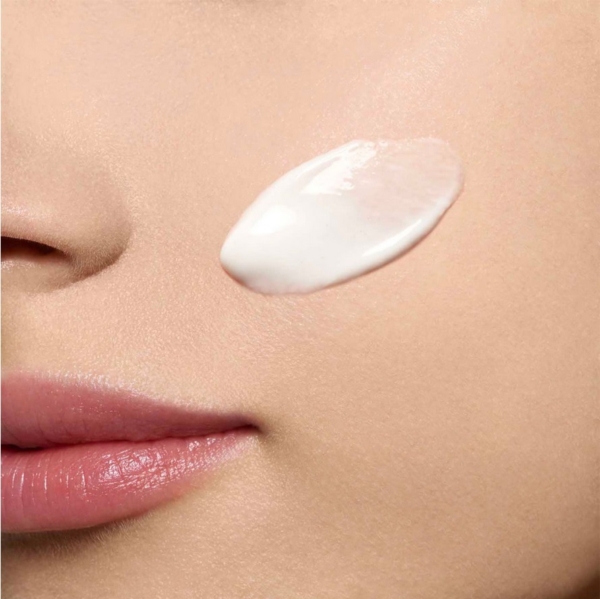 Gros plan sur le visage d'une personne à la peau lisse, avec une large touche d'Emulsion Hydratante Anti Taches Bright Plus 75 ml de Clarins appliquée sur la joue, près des lèvres et du nez. Dakar
