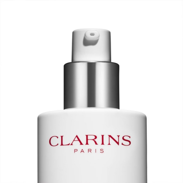 Gros plan sur un flacon blanc de 75 ml de l'Emulsion Hydratante Anti Taches Bright Plus de Clarins avec une pompe argentée, partiellement visible sur un fond blanc uni. La mention "Clarins Paris" apparaît en caractères gras et rouges sur le flacon. Dakar