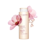 Un flacon de sérum corporel Renew-Plus de Clarins est représenté avec de délicates fleurs roses et des bulles de sérum translucides autour de lui, soulignant la fraîcheur et le soin de la peau. Dakar