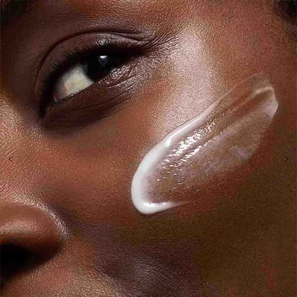 Un gros plan montre le passage du Sérum Expert Éclat Anti Taches Bright Plus Advanced 30 ml sur la joue d'une personne, mettant en valeur sa peau lisse et éclatante et son regard concentré. Dakar