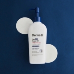 Un flacon blanc de Derma B Huile Réparatrice Corps avec des Céramides CeraMD Repair Oil 200 ml avec une pompe bleue repose sur une surface bleu foncé, avec deux cercles blancs en dessous. L'étiquette comporte un texte en anglais et en coréen. Dakar
