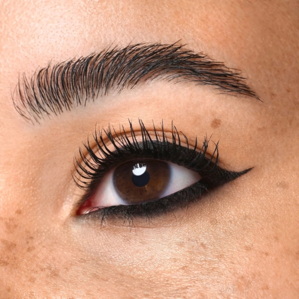 Gros plan sur un œil brun avec de longs cils, un eyeliner noir audacieux et des sourcils bien dessinés, réalisé avec Essence Cadeau Maquillage I Love Extreme Eye 4 pièces. La peau est naturelle et les taches de rousseur sont visibles. Dakar