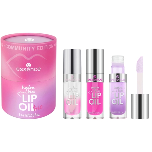 Une boîte cylindrique rose étiquetée "Essence Coffret Cadeau Trio d'Huiles à Lèvres Hydra Kiss 3 x 4 ml" se trouve à côté de trois petits flacons d'huile à lèvres dans les tons clair, rose et lilas, dont l'un présente son applicateur éponge. Dakar