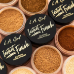 Les contenants ouverts de L.A Girl Poudre Libre de Fixation Instant Finish Blurring Loose Powder 6 g sont disposés côte à côte, affichant des nuances allant du beige clair au marron foncé. Dakar