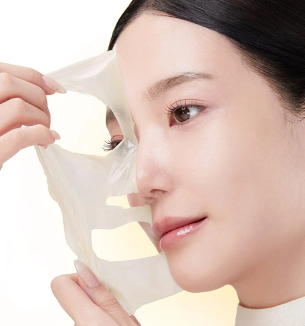 Une femme retire le Medicube Masque de Nuit Révélateur d'Éclat Acide Kojique et Curcuma 75 ml, révélant une peau lisse et éclatante. L'arrière-plan clair met en évidence la clarté de son teint et la douceur du processus de retrait du masque. Dakar