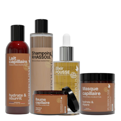 Cinq produits de soins capillaires dans des contenants bruns et beiges sont disposés ensemble. Les bouteilles et les pots sont étiquetés avec des noms tels que "Lait capillaire", "Shampoing RHASSOUL" et "Masque capillaire". Dakar