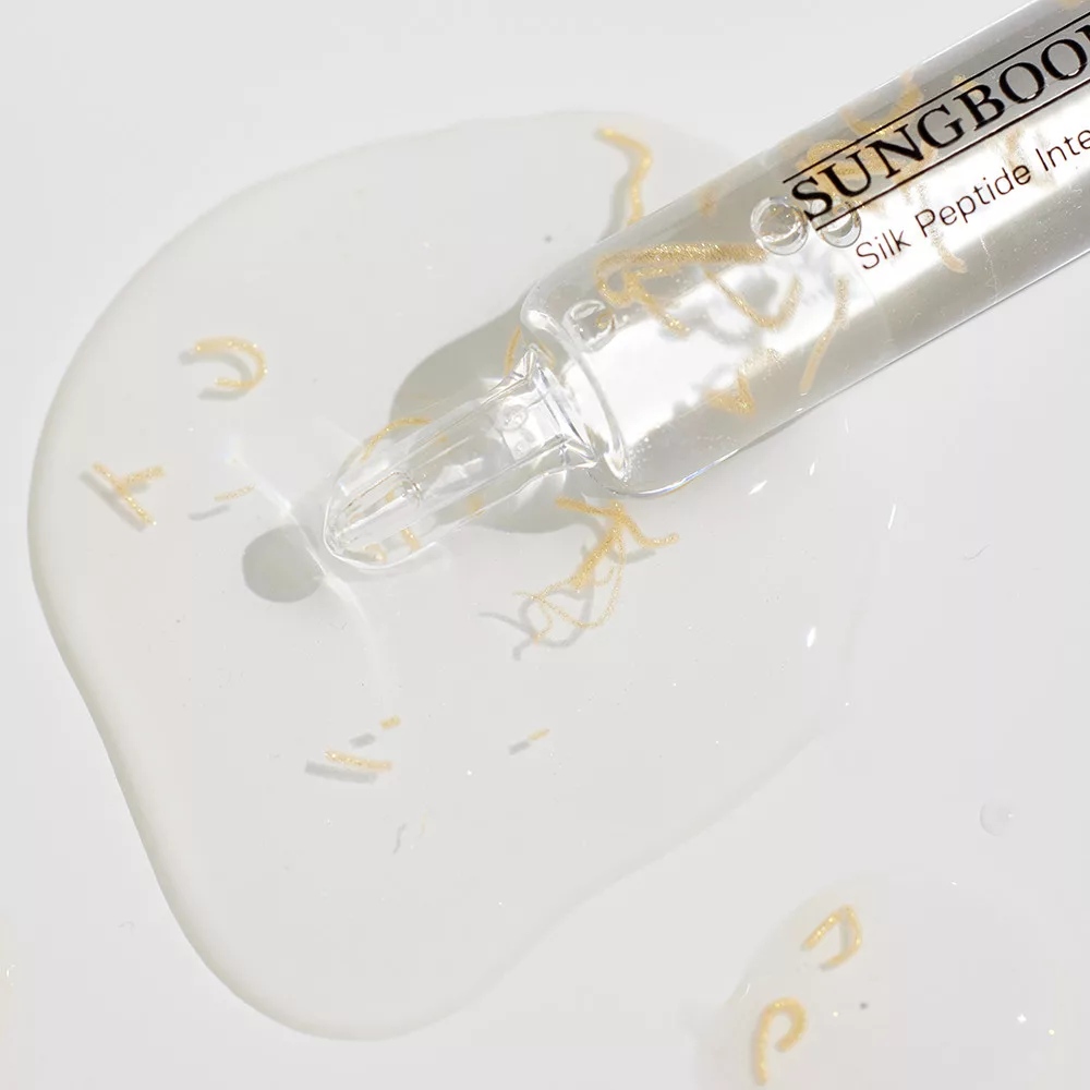 Un compte-gouttes étiqueté "Sungboon Editor Ampoule Anti Age Lifting Intensif aux Peptides de Soie 35ml" libère un sérum transparent avec des mouchetures d'or sur une surface blanche, soulignant le luxe de ce produit de soin infusé aux peptides. Dakar