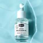 Un flacon transparent de 30 ml de WAAM Sérum Niacinamide 10% avec une pompe blanche repose sur une surface bleu clair avec des gouttes d'eau. L'étiquette française souligne que le sérum est sans parfum et concentré. Dakar