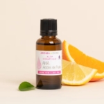 Un flacon brun de 30 ml d'Aroma Zone Actif AHA - acides de fruits se trouve à côté de tranches d'orange et de citron avec une feuille verte sur une surface claire ; il est étiqueté pour un usage cosmétique. Dakar