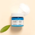 Un pot bleu d'Aroma Zone Actif Niacinamide Soin de la Peau 20g repose sur une surface beige clair, à côté d'une feuille verte et d'un coton blanc. Dakar