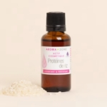 Un flacon en verre brun d'Aroma Zone Actif Protéines de Riz hydrolysées 30ml avec un bouchon noir se trouve à côté d'un petit tas de riz non cuit sur un fond beige clair. Dakar