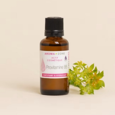 Un flacon en verre brun d'Aroma Zone Actif Provitamine B5 (Panthénol) Peau et Cheveux 30ml se trouve à côté d'une petite plante verte sur un fond beige clair. Dakar