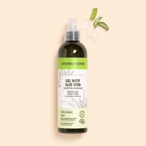 Un flacon de 250 ml d'Aroma Zone Gel natif d'Aloe Vera BIO avec une étiquette verte se tient debout sur un fond beige, à côté de deux gouttes de gel et de deux feuilles d'aloès vertes. Dakar