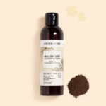 Un flacon d'Aroma Zone Huile de Chébé (macérat huileux) 200ML se tient debout sur un fond beige, avec deux gouttes d'huile et un petit tas de poudre brune à côté. L'étiquette indique clairement le nom du produit et ses caractéristiques. Dakar