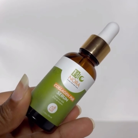 Une main tient un flacon compte-gouttes marron étiqueté "Bionora Sérum Éclat au Collagen Pur Rajeunissant Peau 30 ml" avec un emballage vert et blanc et un bouchon doré sur un fond uni. Dakar