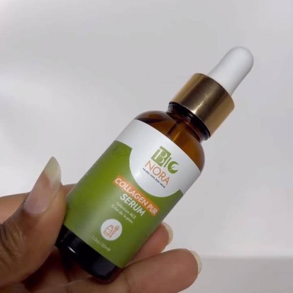 Une main tient un flacon compte-gouttes marron étiqueté "Bionora Sérum Éclat au Collagen Pur Rajeunissant Peau 30 ml" avec un emballage vert et blanc et un bouchon doré sur un fond uni. Dakar