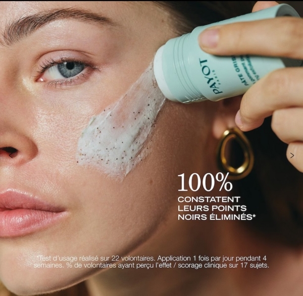 Une femme utilise le Payot Stick Exfoliant Gommant Purifiant Visage 25 g - un exfoliant crémeux aux grains visibles - sur sa joue. L'étiquette du stick porte la mention "PAYOT", et le texte français met en évidence les détails relatifs à l'élimination des points noirs et aux tests d'utilisation. Dakar